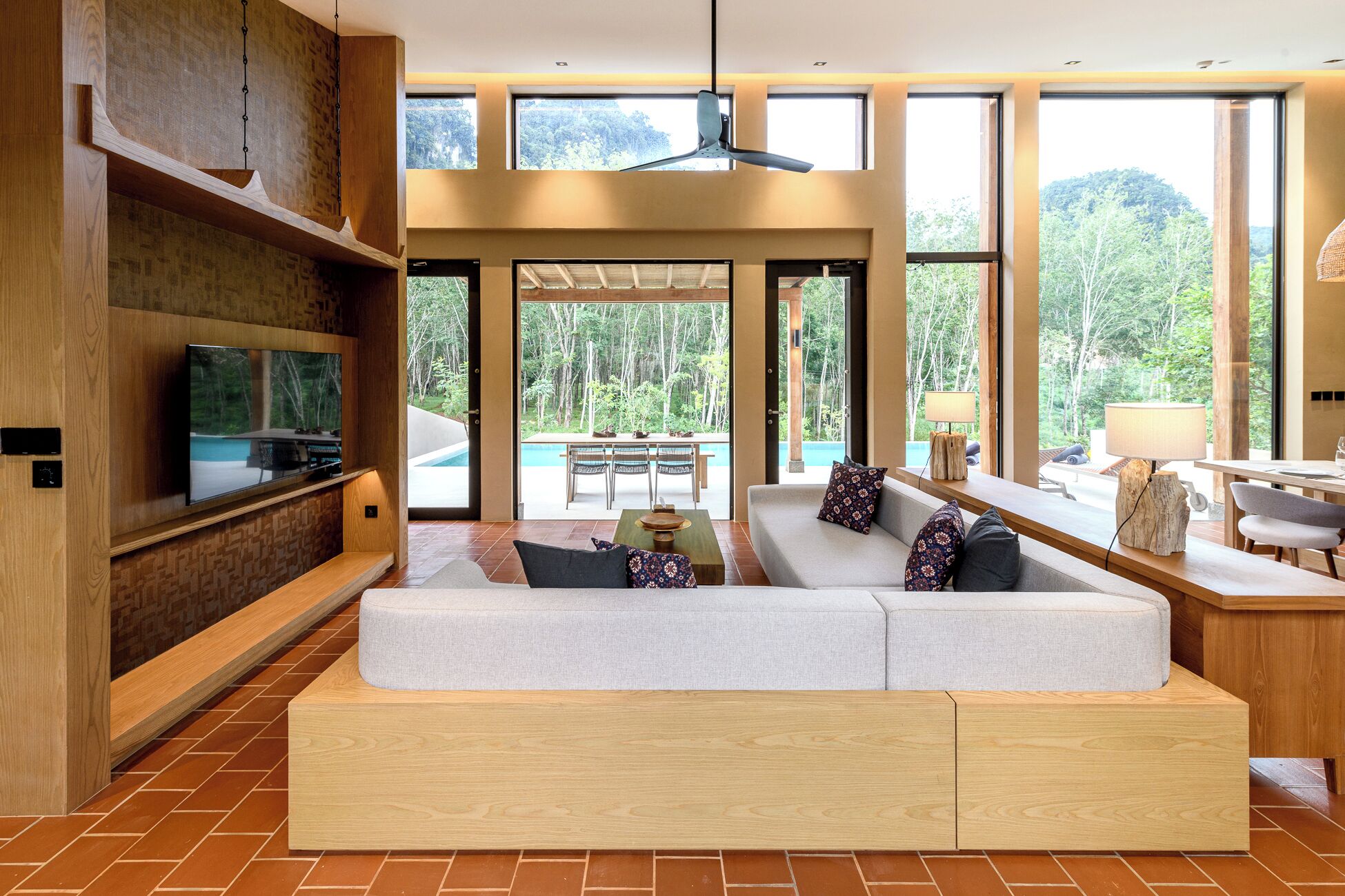 Una sala de estar moderna con sofá empotrado, televisor de pantalla plana y comedor con vista a la piscina.