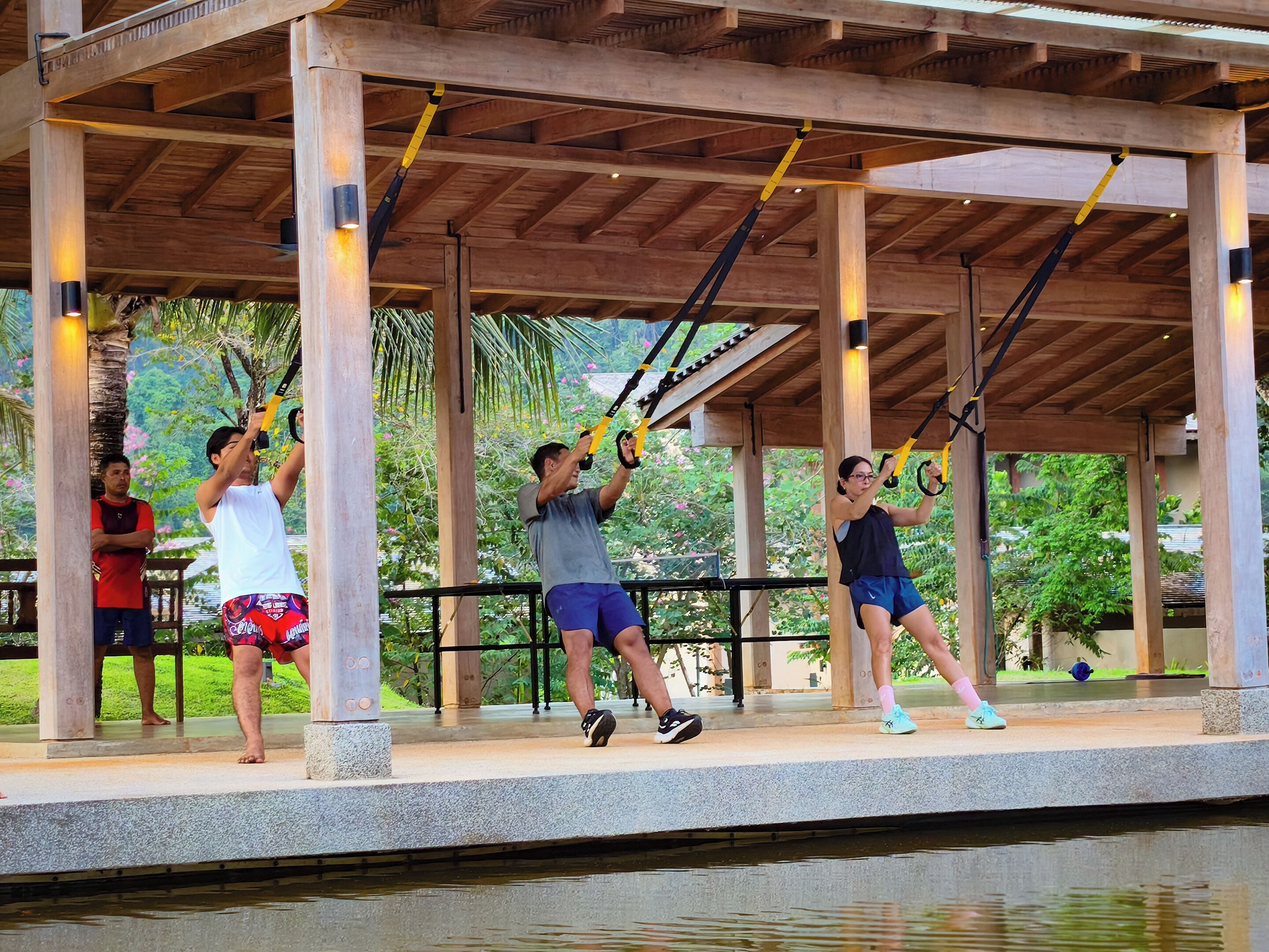 A covered outdoor area with wooden beams and pillars, a water feature, and exercise equipment.