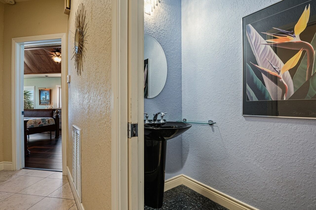 A bathroom with a black sink, a round mirror, and a framed abstract painting on the wall.