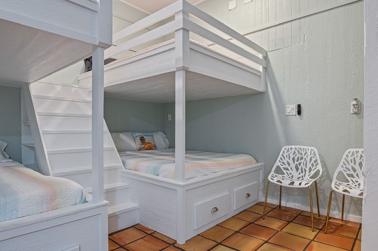 Une chambre avec un lit superposé, un petit bureau et deux chaises blanches.