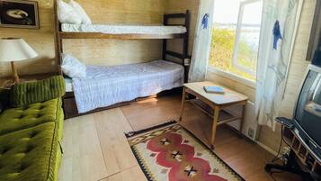 A room with bunk beds, a green sofa, a small table with a book, a television, and a window with curtains.