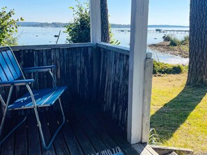 A wooden deck with two blue chairs, overlooking a calm body of water with a pier in the distance. - 4 Person Holiday Home in Onsala (Gottskar)