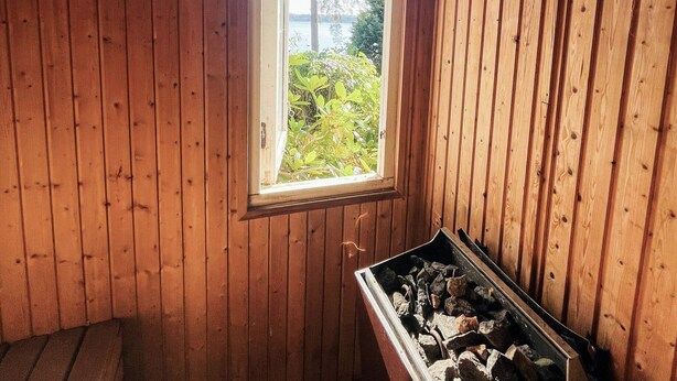 A room with wooden walls, a window, and a fireplace with logs. - 4 Person Holiday Home in Onsala (Gottskar)