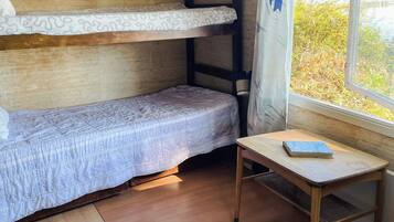 Um quarto pequeno e acolhedor com uma cama beliche, uma cama de solteiro e uma mesinha com um livro.