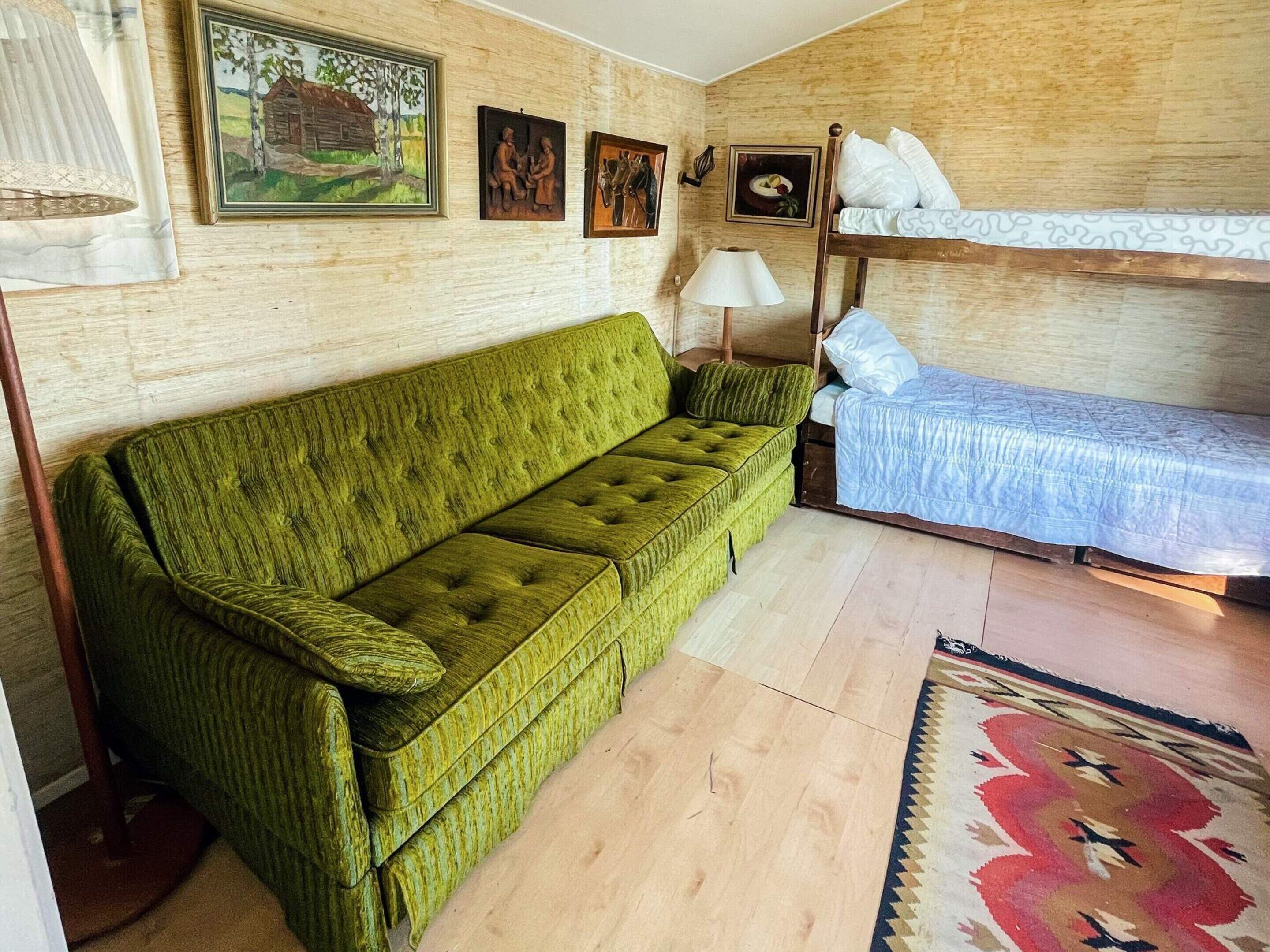 A room with a green sofa, a bunk bed, a lamp, and a rug.