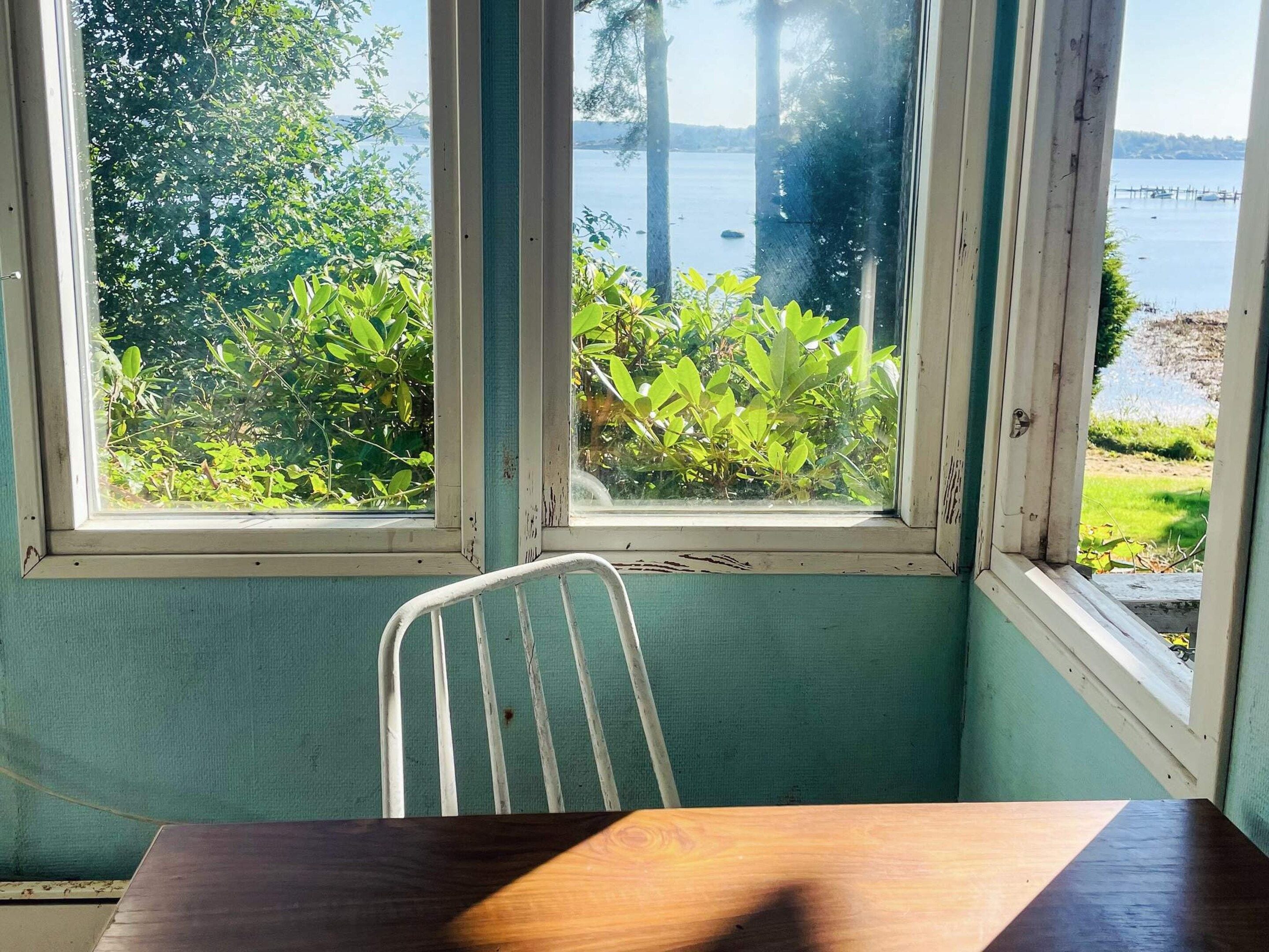 A room with a view of a lake, a metal chair, and a wooden table.