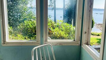 A room with a view of a lake, a metal chair, and a wooden table.