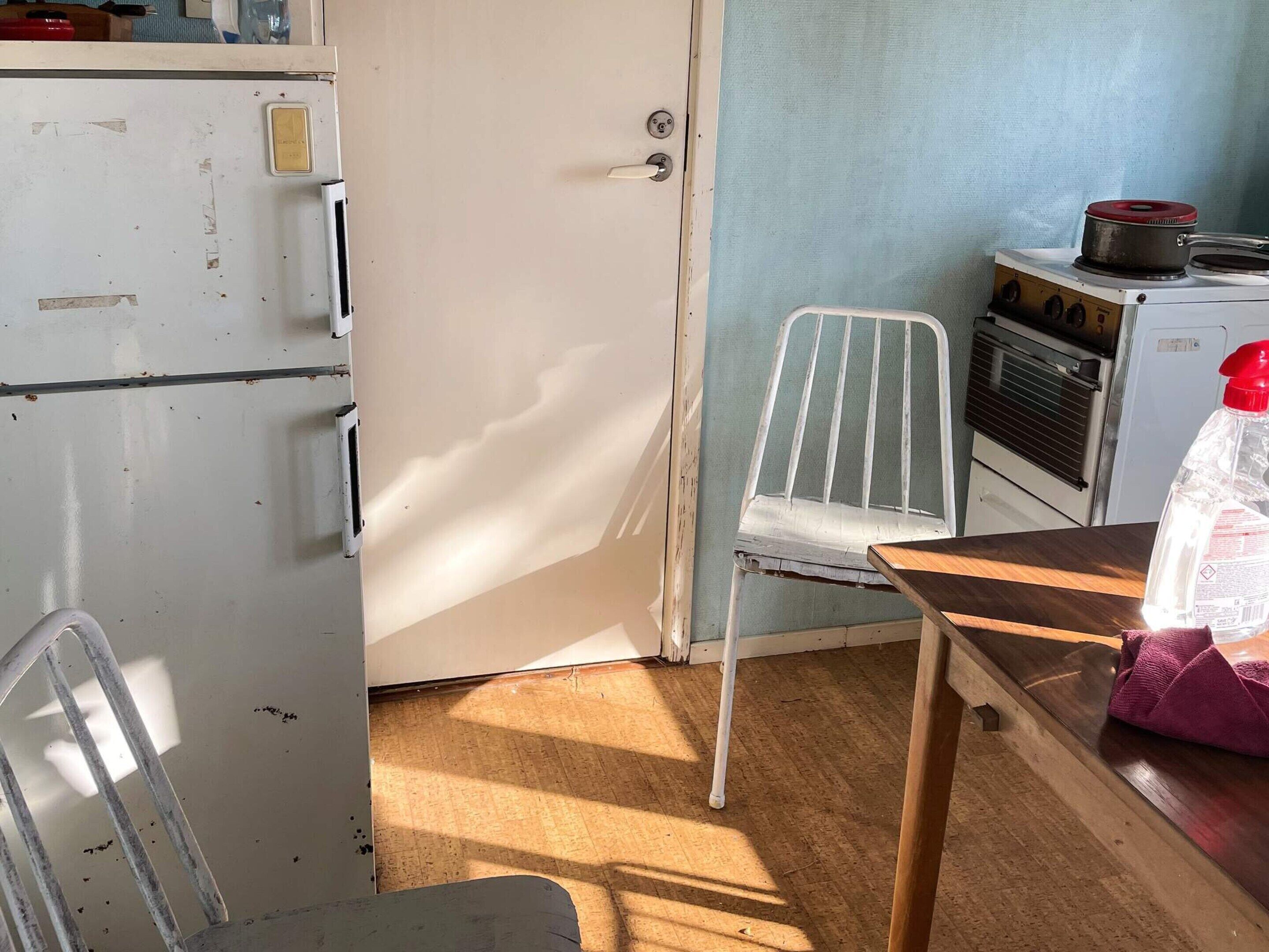 A compact kitchen with a white refrigerator, a stove, and a chair.
