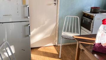 A compact kitchen with a white refrigerator, a stove, and a chair.
