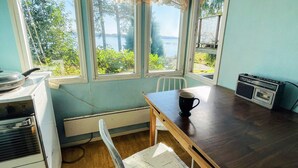 A room with a wooden table, a white chair, a radio, and a view of a lake through large windows. - 4 Person Holiday Home in Onsala (Gottskar)
