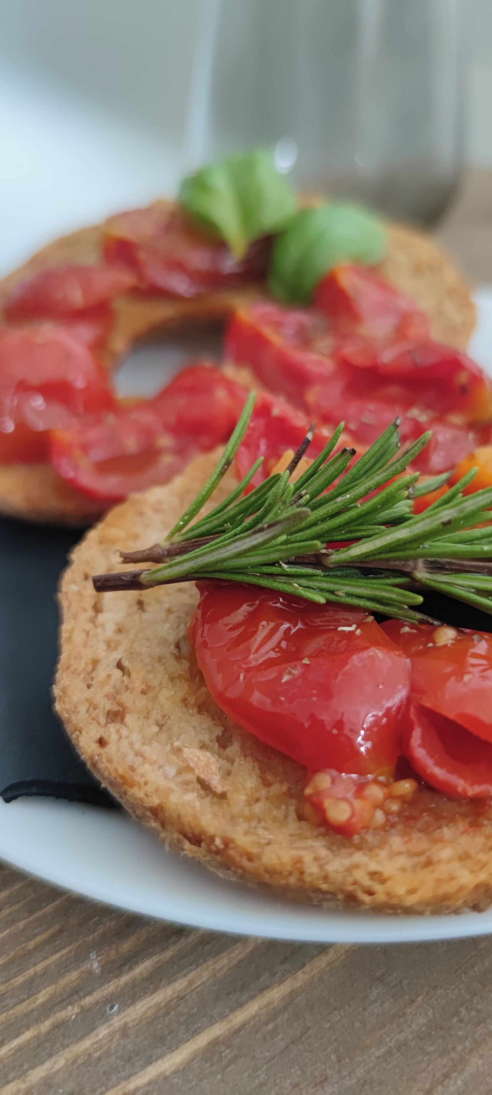 Un plato con dos sándwiches abiertos, cubiertos con rodajas de tomate y una ramita de romero.