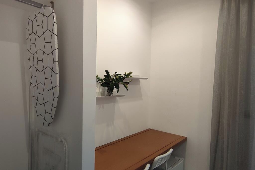A bathroom with a white wall, a wooden bench, a white chair, and a plant on a shelf.