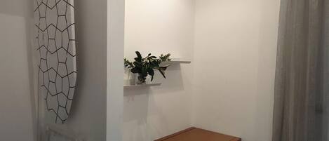 A bathroom with a white wall, a wooden bench, a white chair, and a plant on a shelf.