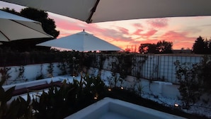 A patio area with umbrellas and a view of a sunset over a garden.
