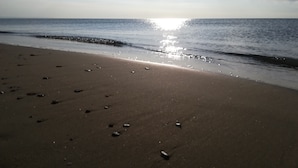 A beach with footprints leading to the water, a clear sky, and the sun reflecting on the water.