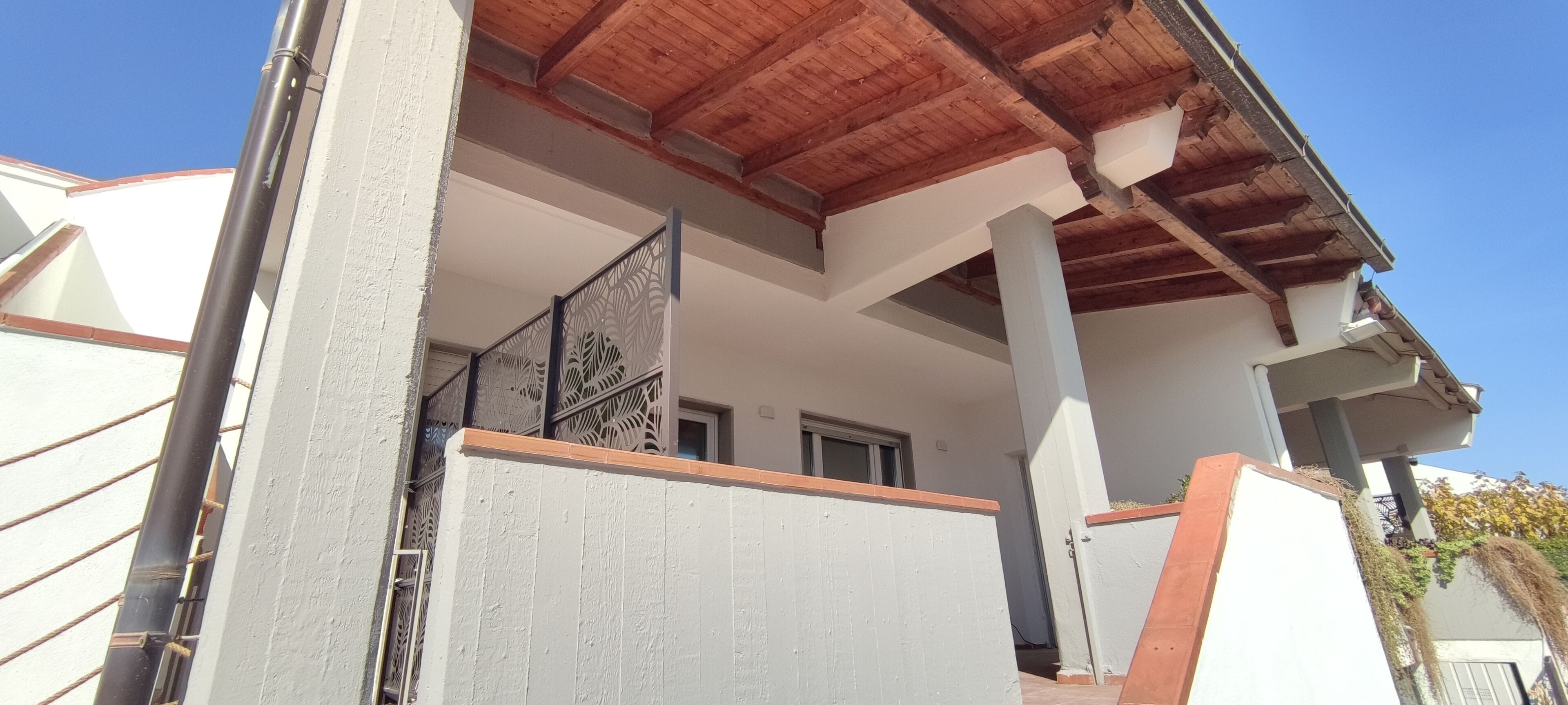 A residential building with a balcony, a wooden ceiling, and a white exterior wall.