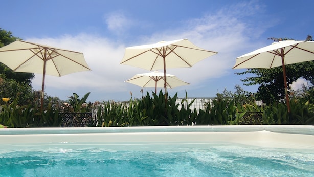 A swimming pool with three white umbrellas and lush greenery in the background.