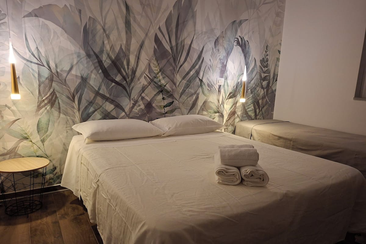 A hotel room with a large bed, two bedside tables, a small round table, and a wall with a leafy pattern.