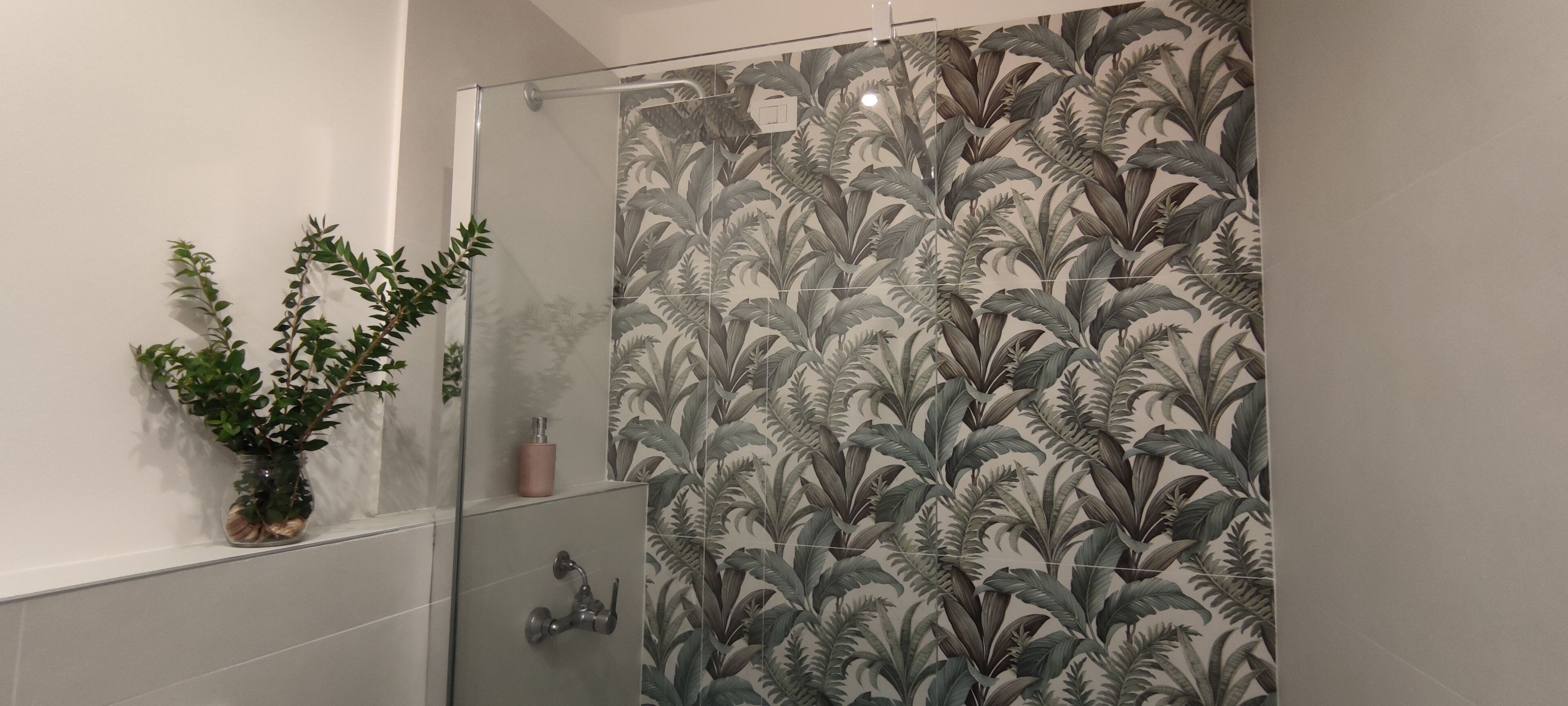 Une salle de bain avec une douche à parois de verre, une plante en pot et un porte-rouleau de papier toilette.
