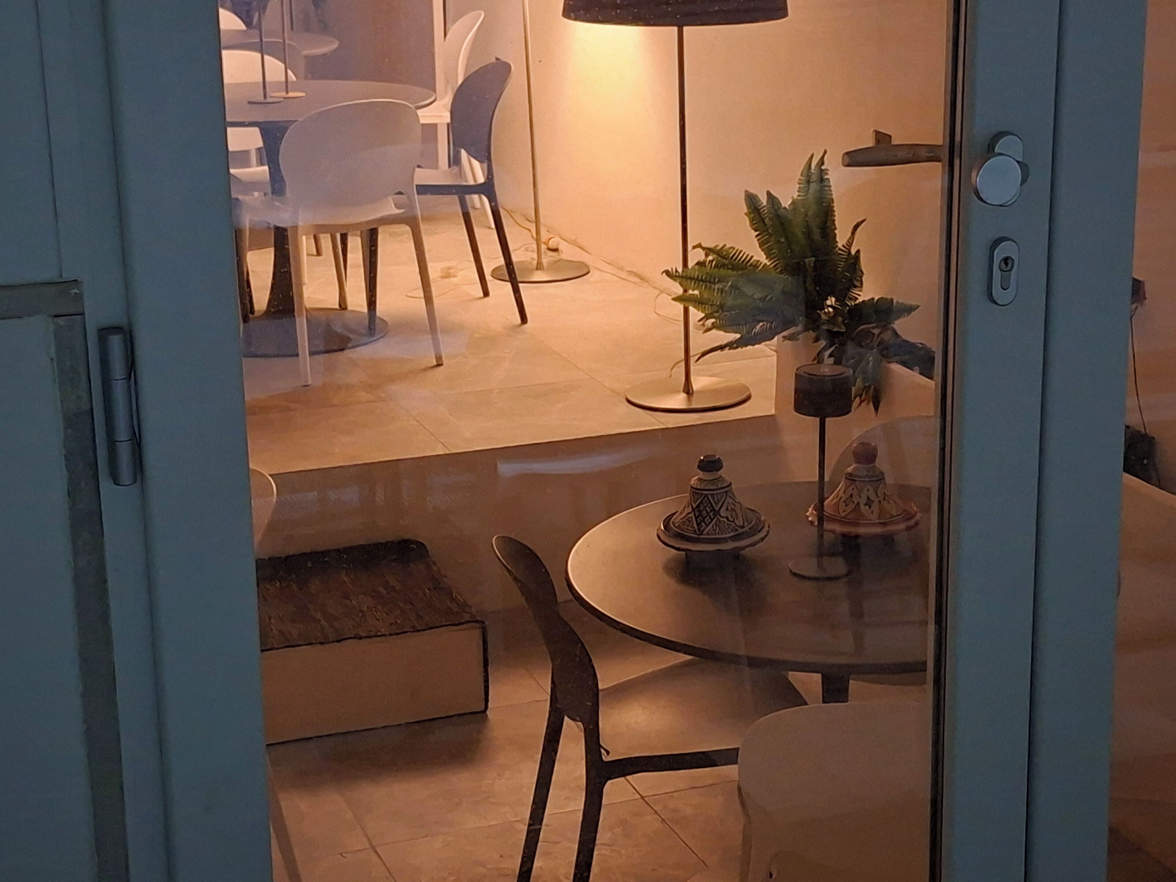 Uma sala de jantar com uma mesa redonda, cadeiras, um vaso de planta e um abajur.