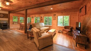A wooden cabin interior with a sofa, armchairs, a dining table, and a TV. - Pet-Friendly Classic Maine Camp on Quiet Coffee Pond (Casco)