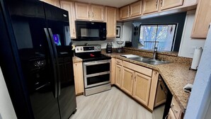 A compact kitchen with a microwave, oven, and refrigerator. It features light wood cabinets and a skylight above the countertop. - Great Location 2 BR, 2 Bath condo in quiet community, MINUTES from the beach!!   (Fort Myers)