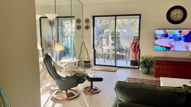 A modern living room with a black leather sofa, a glass dining table, and a television mounted on the wall. - Great Location 2 BR, 2 Bath condo in quiet community, MINUTES from the beach!!   (Fort Myers)