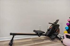 A stationary bike, a set of dumbbells, and a kettlebell in a room with a wooden floor and a white wall.
