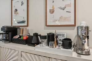 A coffee station with a coffee maker, cups, and a sign that reads "COFFEE."