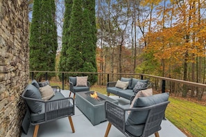 An outdoor seating area with a fire feature, stone wall, and tall trees.