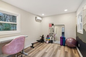 A room with a desk, exercise equipment, a mirror, and a window.