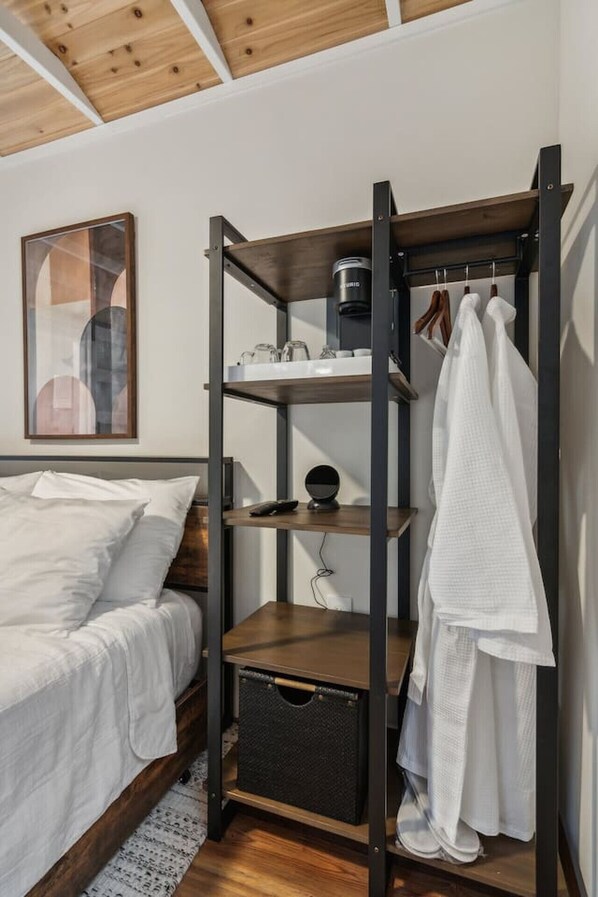 A bedroom with a bed, a wooden shelf unit with storage, a hanging robe, and a framed picture on the wall.