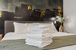 A neatly made bed with white linens and a stack of folded towels.