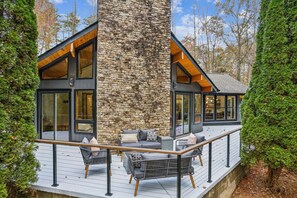 A modern house with a stone facade, large windows, and a wooden deck with outdoor furniture.