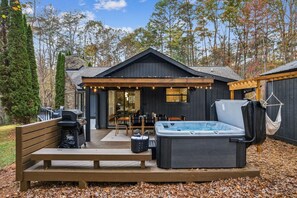 Eine Holzterrasse mit Whirlpool, Grill und einer Sitzgruppe im Freien.