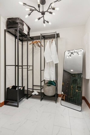 A corner room with a black metal shelving unit, a mirror, and a hanging light fixture.
