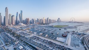 Un paysage urbain avec des gratte-ciel modernes, une marina remplie de bateaux et une grande structure circulaire visible au loin.