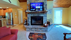 Ein Wohnzimmer mit Kamin aus Stein, einem flachbildfernseher darüber und einem roten Sofa.