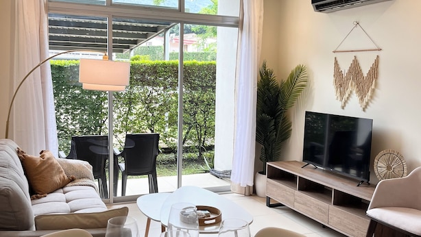 A modern living room with a large TV, comfortable seating, and a dining area set for a meal. - Prime Location 2 BDR Apt, Pool, GYM, ground floor, Walkable to Everything (Santa Ana)