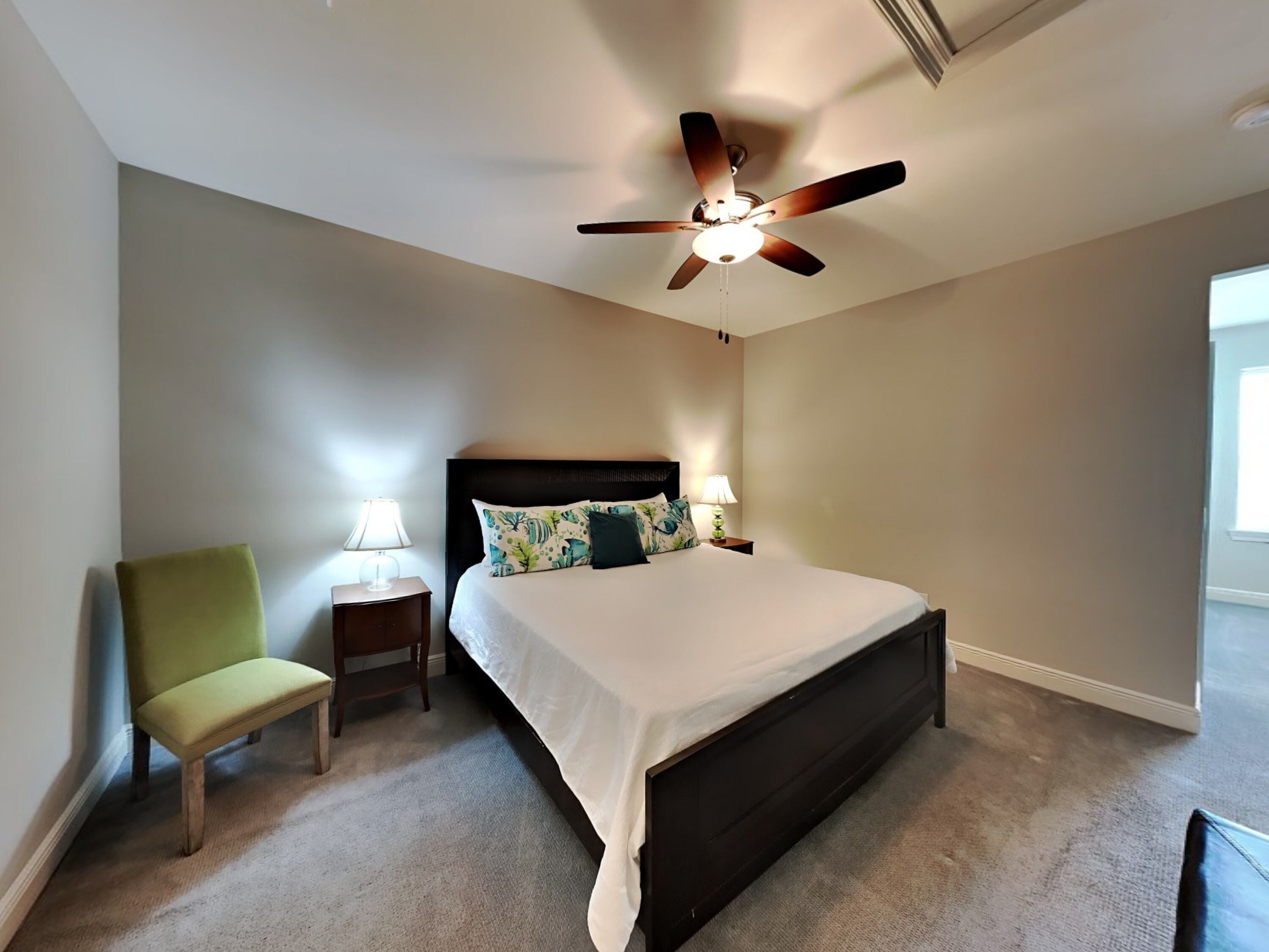 A bedroom with a bed, a chair, a nightstand, a ceiling fan, and a window.
