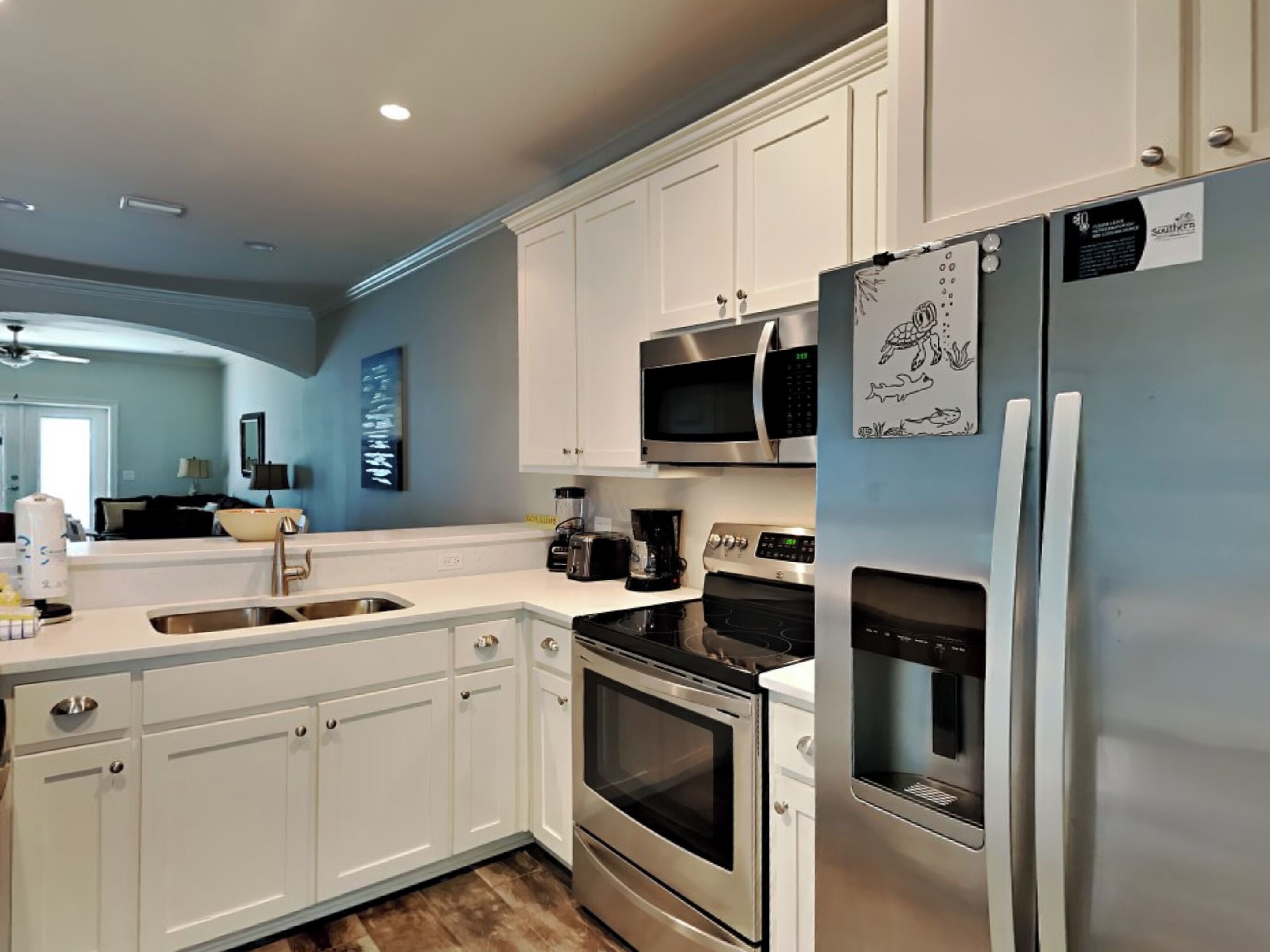 A modern kitchen with white cabinets, stainless steel appliances, and a blue accent wall.
