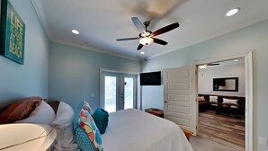 A bedroom with a bed, pillows, a ceiling fan, a TV, and a door leading to another room. - Banana Bay Townhome #13909 by Southern Vacation Rentals (Pensacola)