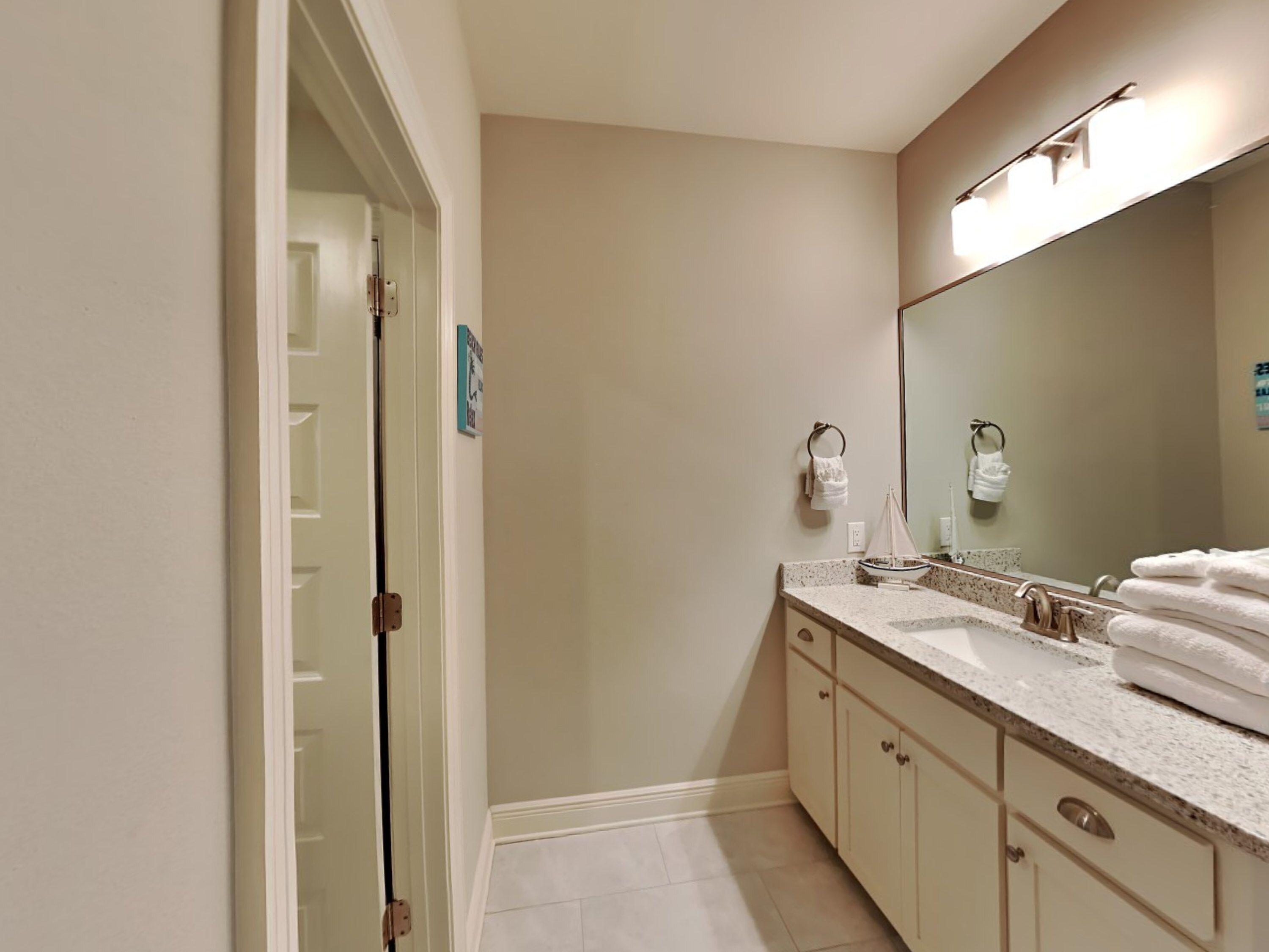 A bathroom with a large mirror, two sinks, a towel rack, and a door leading to a shower area.