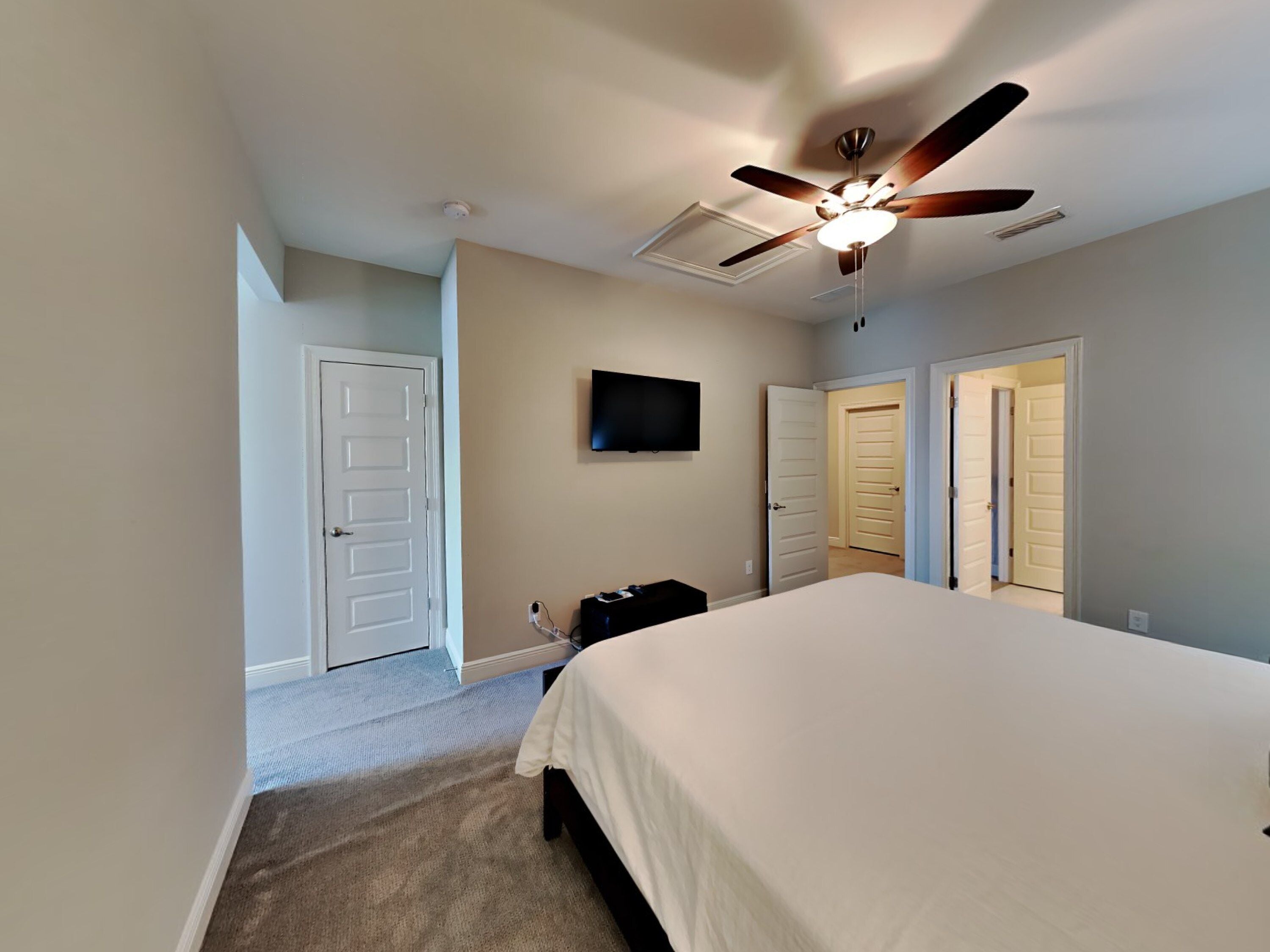 A bedroom with a bed, a ceiling fan, a TV, and two doors.