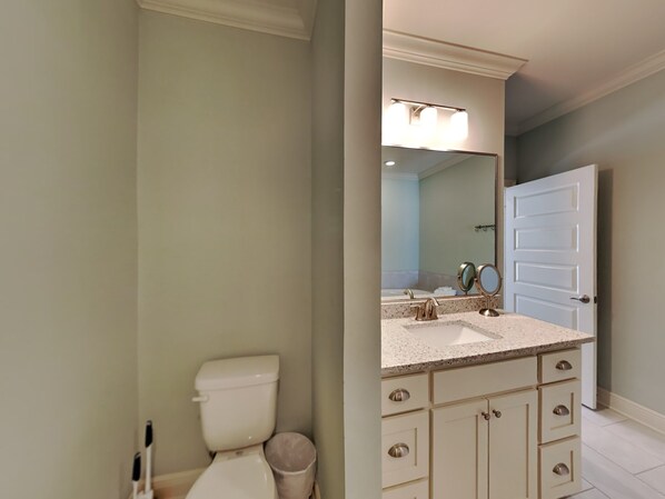 A bathroom with a toilet, sink, vanity, and a mirror.