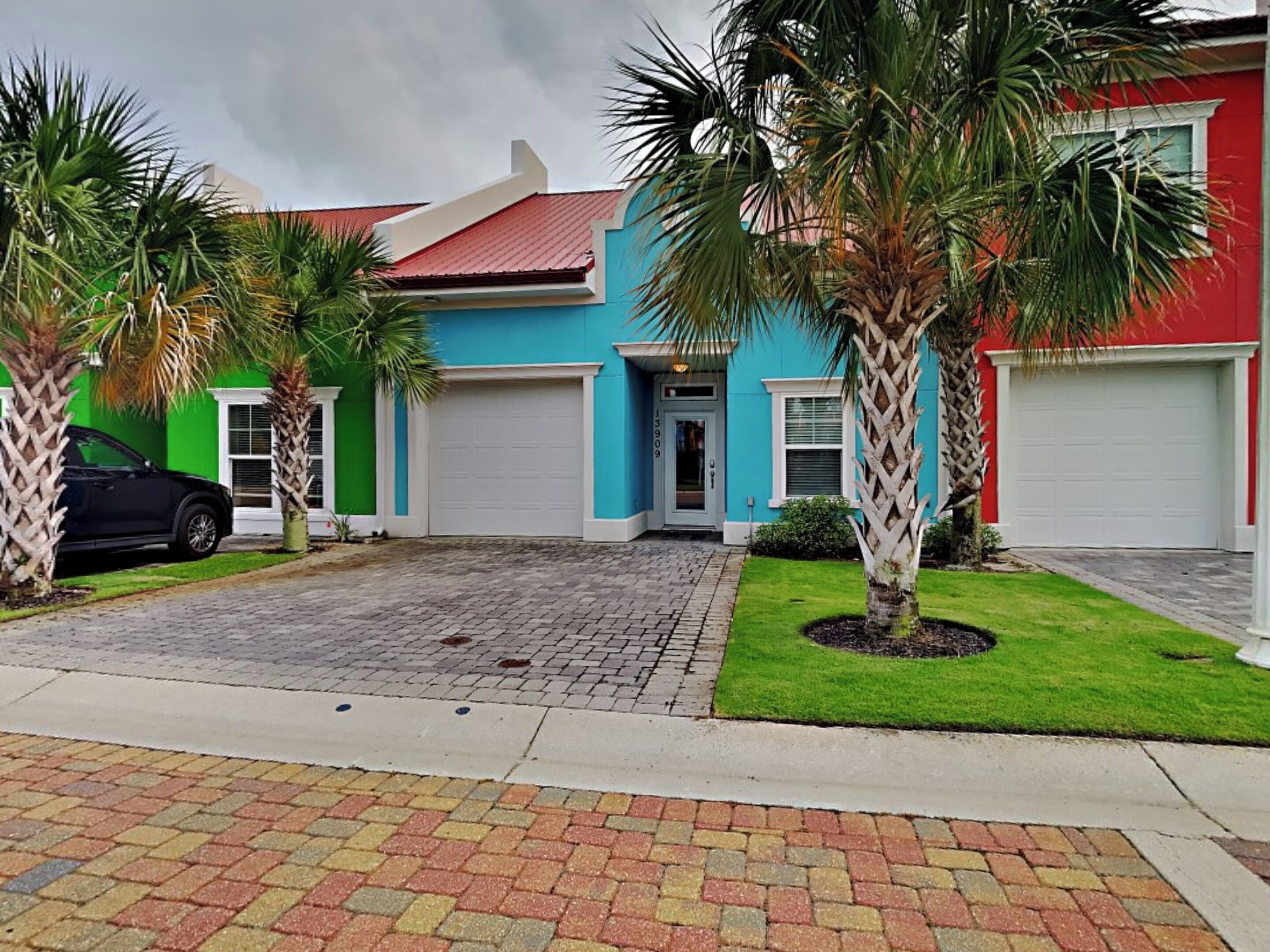 A two-story house with a blue and red exterior, a driveway, and two palm trees.