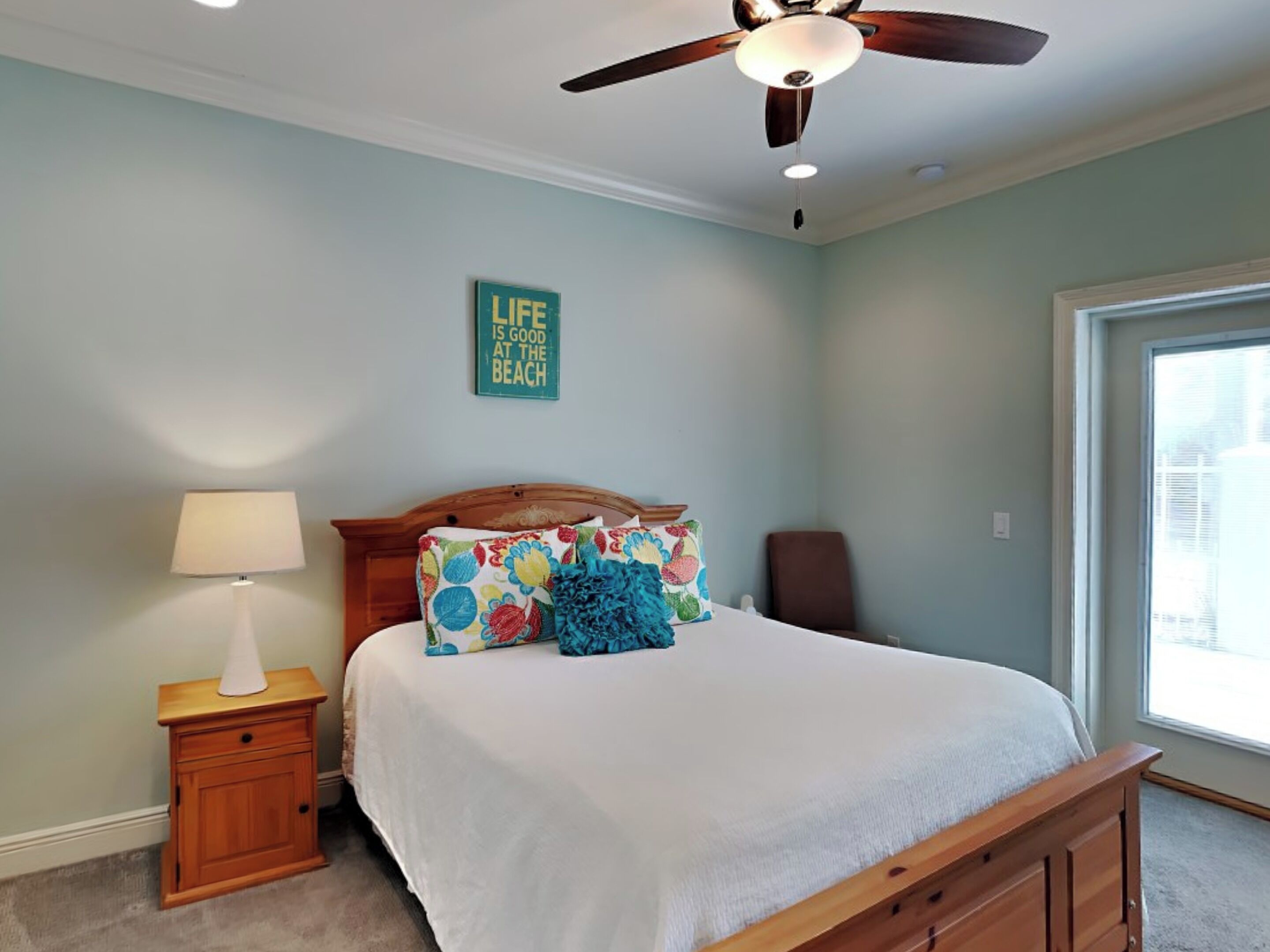 A bedroom with a bed, a nightstand, a lamp, a ceiling fan, and a window.