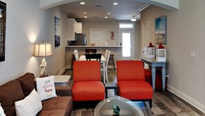 A living room with a brown sofa, two red chairs, a glass coffee table, and a kitchen in the background. - Banana Bay Townhome #13909 by Southern Vacation Rentals (Pensacola)