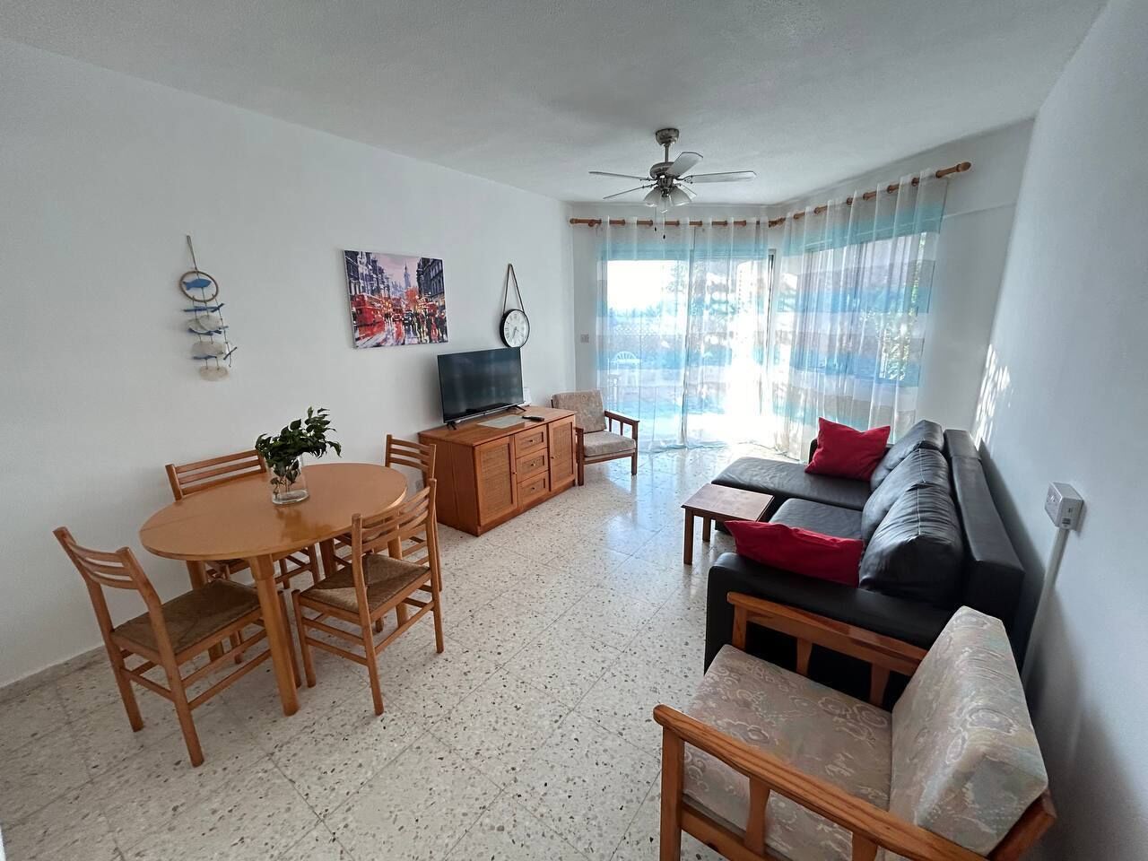 Una sala de estar con una mesa de comedor, sillas, un sofá, un televisor y un ventilador de techo.