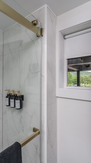Une salle de bain moderne avec un mur en marbre, une douche en verre et une fenêtre donnant sur un paysage verdoyant.